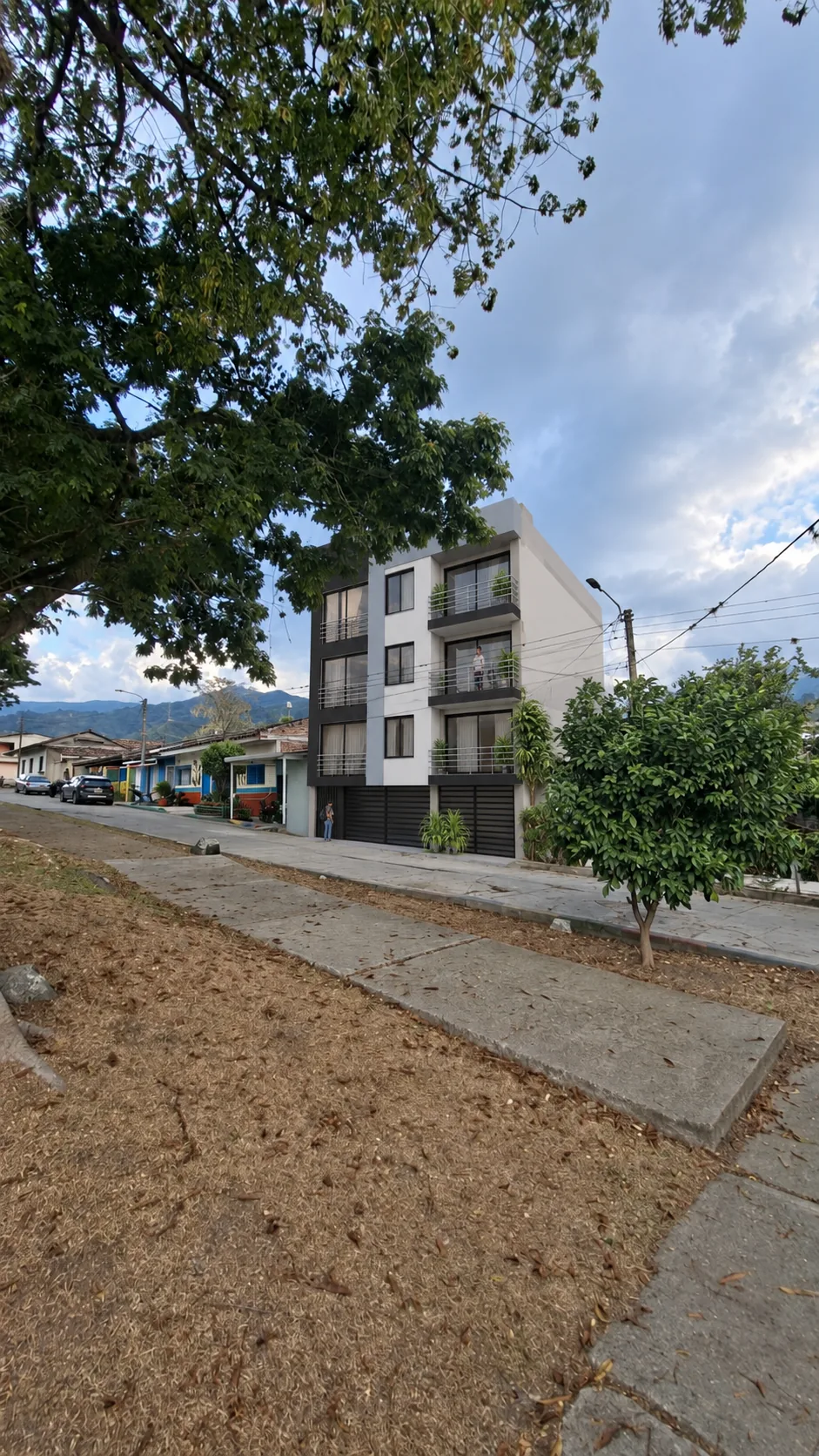 El edificio visto desde el parque principal de La Magdalena, con la calle, las casas de la vereda y las montañas al fondo